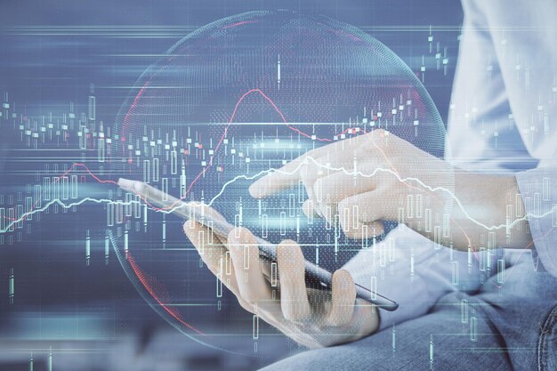 Double exposure of man's hands holding and using a digital device and forex graph drawing financial market concept