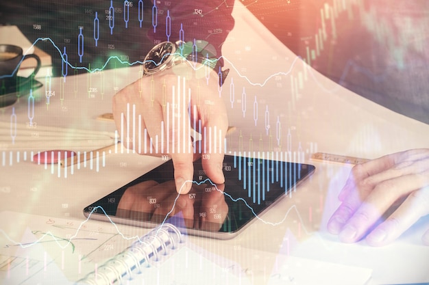 Double exposure of man's hands holding and using a digital device and forex graph drawing Financial market concept