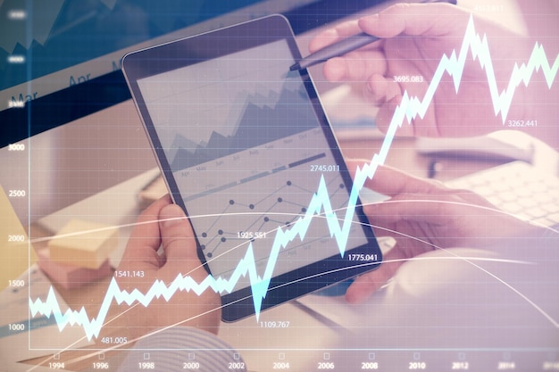 Double exposure of man's hands holding and using a phone and financial chart drawing Market analysis concept