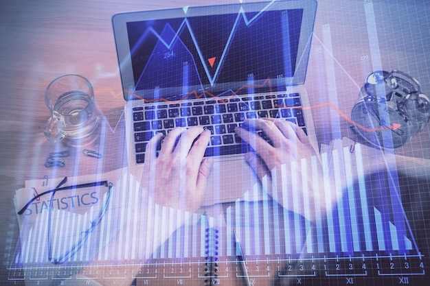 Double exposure of man's hands typing over laptop keyboard and forex chart hologram drawing Top view Financial markets concept