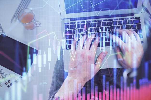 Double exposure of man's hands typing over laptop keyboard and forex chart hologram drawing Top view Financial markets concept