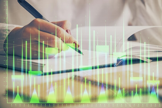 Double exposure of woman's hands making notes with forex graph hologram Concept stock market analysis