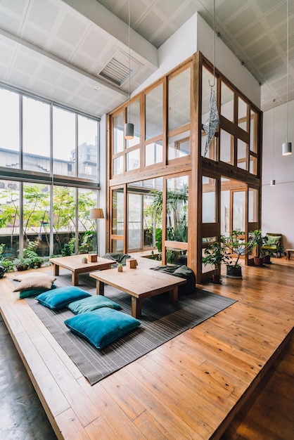 Double space hall decorated with wood inside hostel public area\
with low tables, bean bags and pillows.