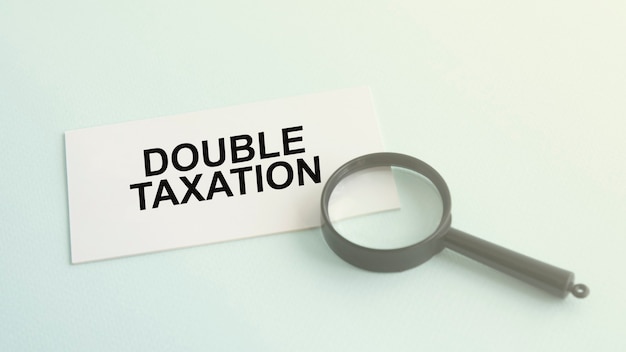 Double taxation word on white paper card and magnifying lens