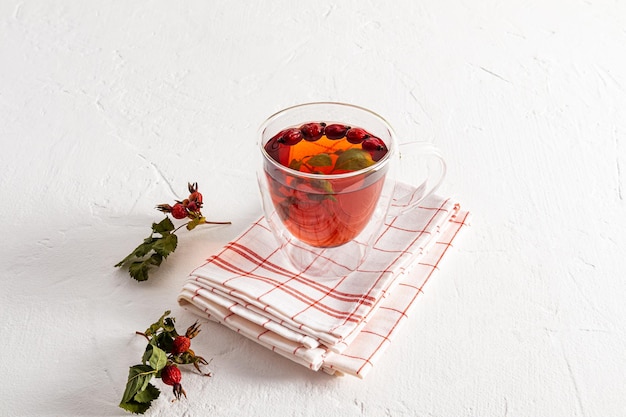 A doublebottomed glass cup with hot rosehip broth stands on a towel and a white table prevention and treatment of avitominosis increased immunity