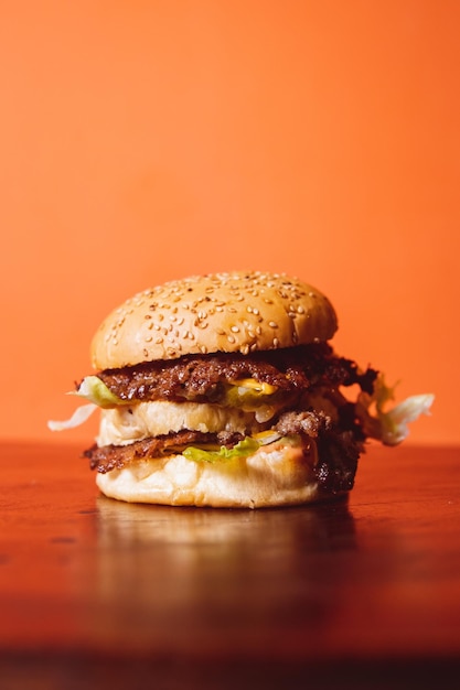 Doubledecker burger on top of a wooden table with an orange background