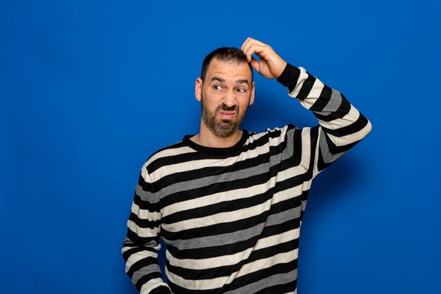 Doubtful bearded hispanic man thinking scratching his head trying to find a solution isolated on a blue background person