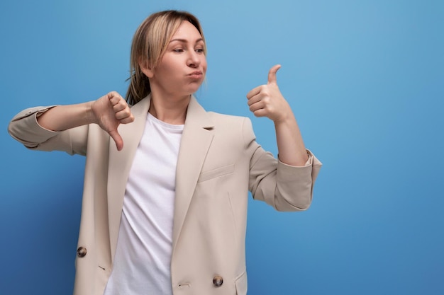 Doubtful blonde young adult in beige jacket on studio background with copy space