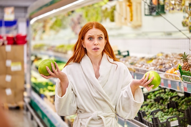 Donna dubbiosa che sceglie frutta fresca, confronta, sceglie a favore del meglio, pensa