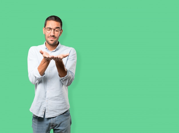 Doubtful young man holding something with his hand