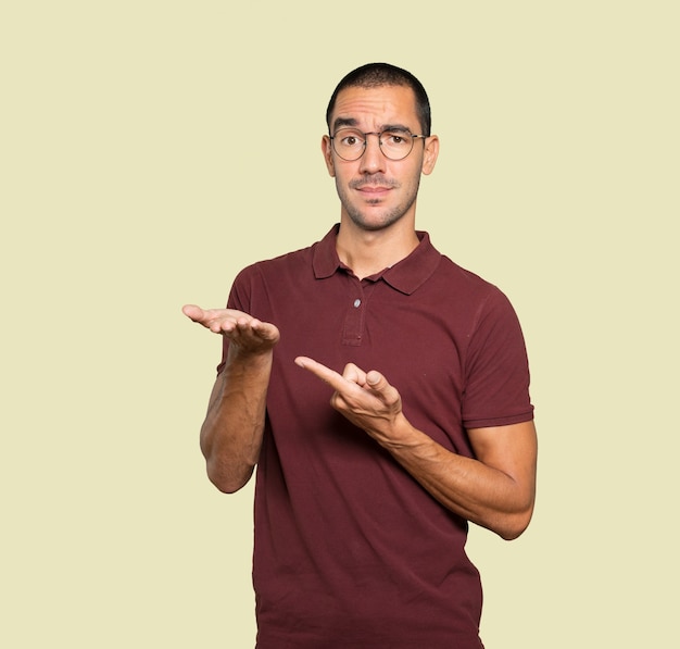 Doubtful young man holding something with his hand