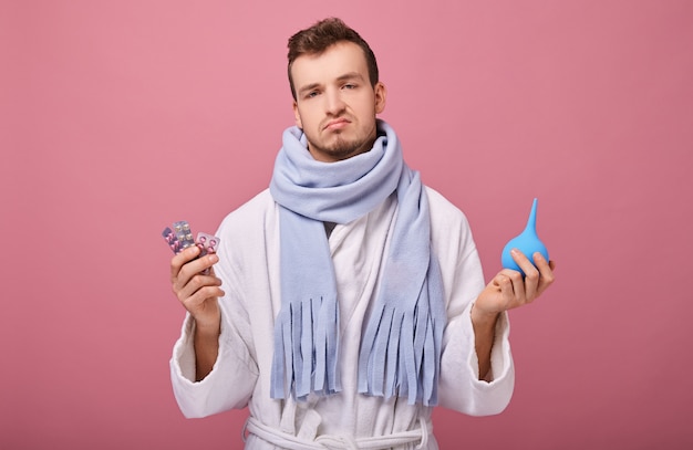 doubting man with poor health in bathrobe and scarf holds enemand pills