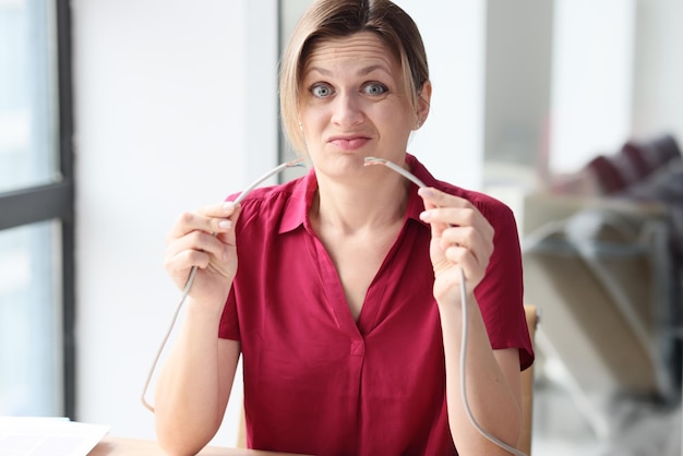 Doubting woman holds teared internet wire sitting at table in office emotional employee worries