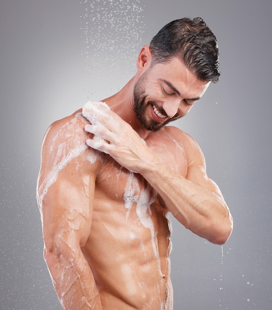 Douchespons en man met water in studio op grijze achtergrond voor wellnessverzorging en schoonheid Huidverzorging badkamerhygiëne en gelukkige mannelijke glimlach voor het wassen van lichaamsreiniging en zeep voor een gezonde huid