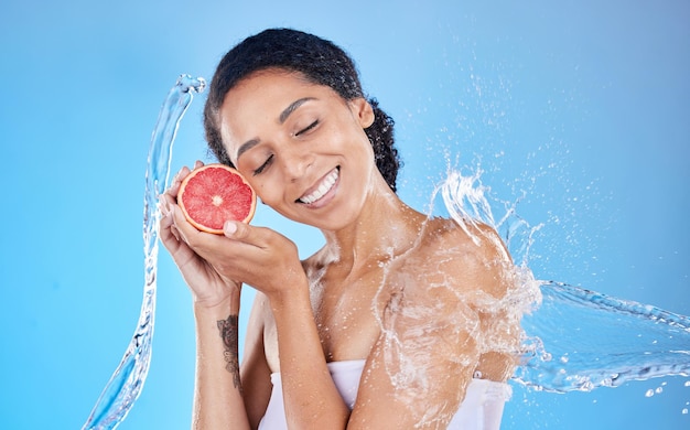 Douchewater en grapefruit met een model zwarte vrouw in studio op een blauwe achtergrond met een plons voor hygiëne Gezondheidswaterplons en huidverzorging met een aantrekkelijke jonge vrouw die natuurlijk fruit vasthoudt