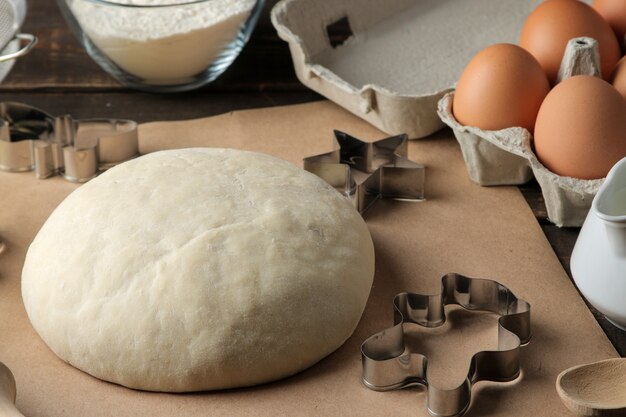 Dough and baking ingredients biscuit forms and baking tools on a brown wooden table.