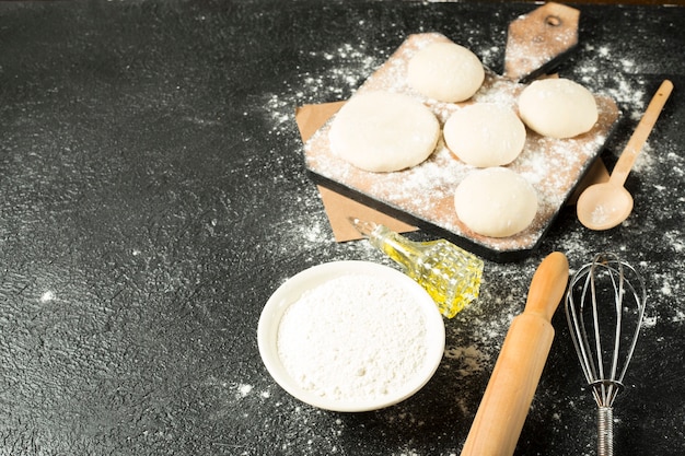 Dough balls on a wooden plate with cooking ingredients on the black background
