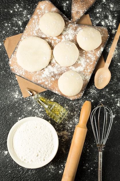 Dough balls on a wooden plate with cooking ingredients on the black table