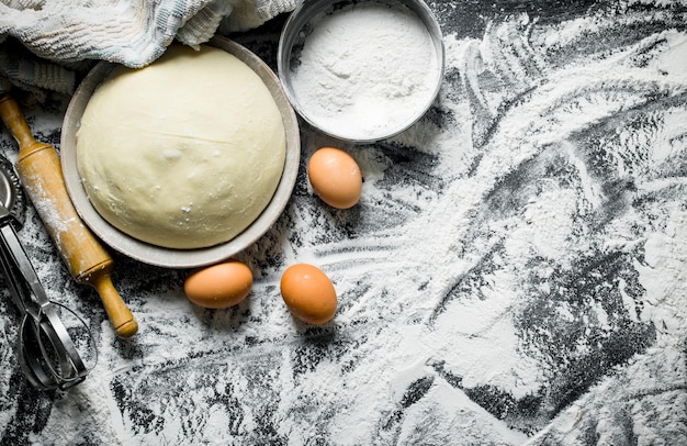 Dough in bowl with eggs rolling pin and flour