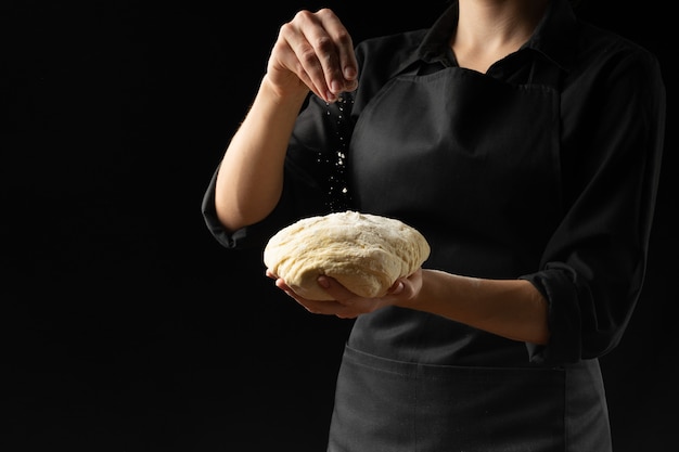 Dough in the hands of the chef's chief with flour on a dark background. 