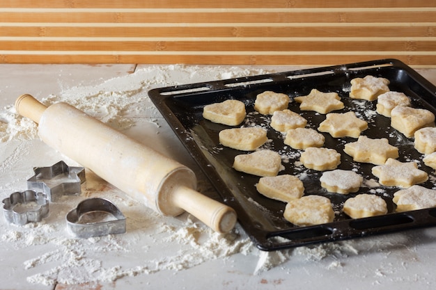 Dough has just been kneaded and made cookies. Cookies lie on a black baking sheet. Rolling pin and cookie cutters on the table. Photorecept. A series of photographs.