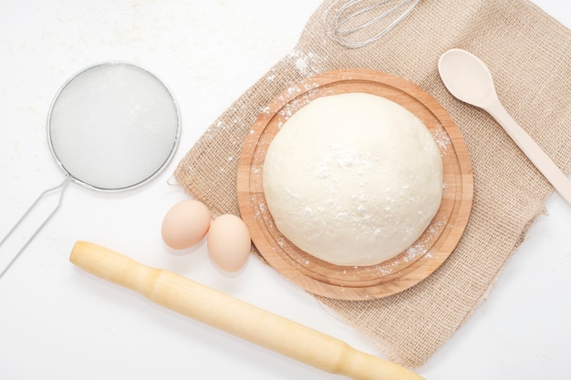 Dough is a close-up view from the top, sprinkled with flour, on the table next to the rolling pin and eggs