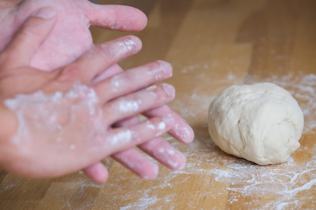 Dough lies on wooden table next to hand in flour, cooking, making pastry and bread, dough kneading