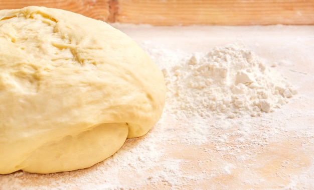 Dough with a pile of flour on a wooden background.