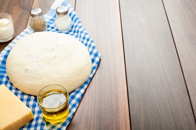 Dough on a wooden table, on a blue kitchen napkin, with olive oil, salt and pepper, and sour cream