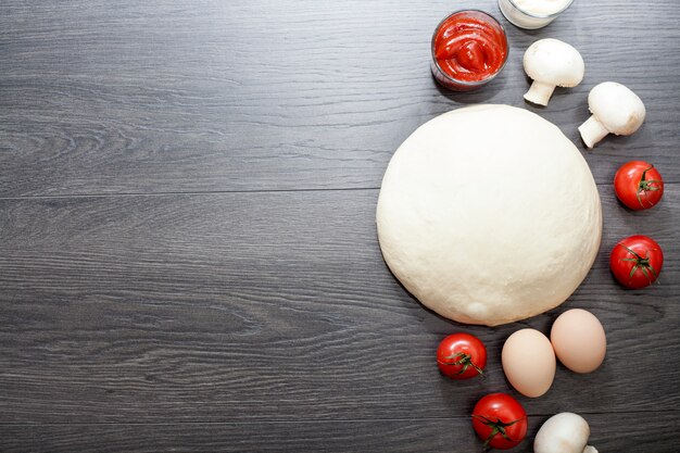 Impasto su un tavolo di legno, accanto a uova, funghi, olio d'oliva, pomodori, sale e pepe