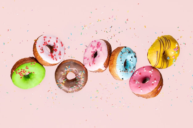 Doughnut collection with flying blue, pink, green and yellow donuts on pink background