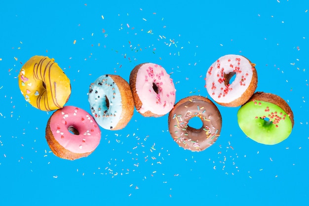 Doughnut collection with flying blue, pink, green and yellow donuts on pink background