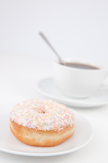 Doughnut with multi coloured icing sugar and a cup of coffee with a spoon on white plates