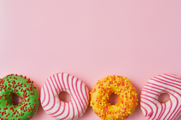 Doughnut with multicolored glaze on trendy pink background. Donut are traditional sweet pastries.