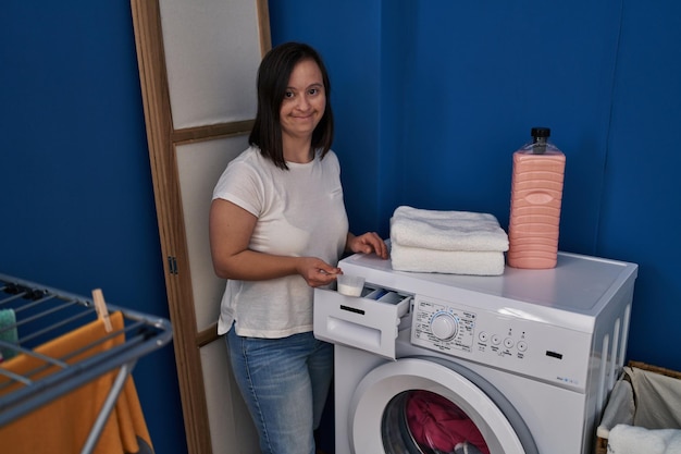 Down syndrome woman smiling confident pouring detergent on washing machine at laundry room