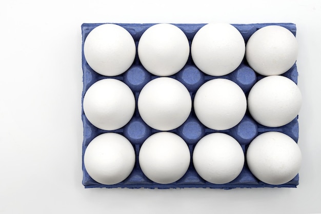 A dozen white chicken eggs in a blue egg cup with white uniform background