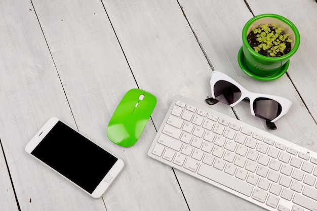 Draadloos slank wit toetsenbord en groene muis smartphone bril bloem op wit houten bureau