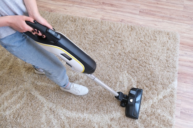 Draadloze stofzuiger wordt gebruikt om het tapijt in de kamer te reinigen. Huishoudelijk werk met een nieuwe handstofzuiger. Huis schoonmaken, zorg en technologie concept.