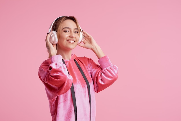 Draadloze verbinding. Portret van het jonge vrouw stellen geïsoleerd over roze het luisteren pretmuziek met hoofdtelefoons.