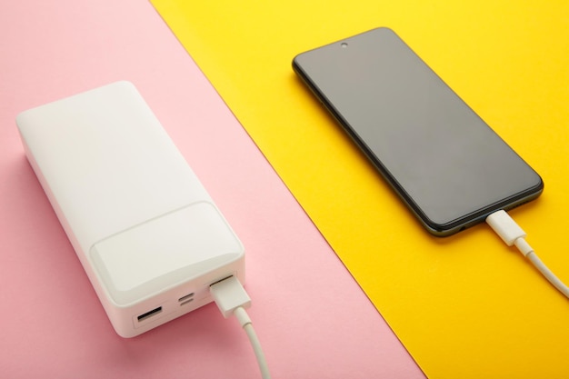 Draagbare powerbank met usb-kabel op roze en gele achtergrond