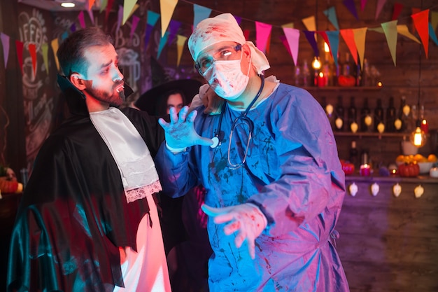 Dracula man looking at his doctor friend while celebrating halloween. Scary doctor at halloween party.