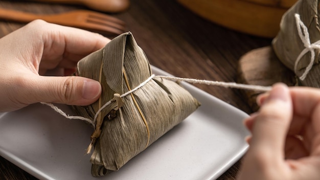 Dragon boat festival food rice dumpling zongzi young asian\
woman eating chinese traditional food on wooden table at home\
celebration close up