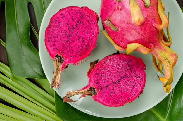 Dragon fruit on a green plate. Dark background with palm leaves.