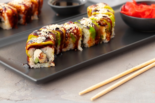 Rotoli di sushi del drago con anguilla e avocado sul tavolo grigio