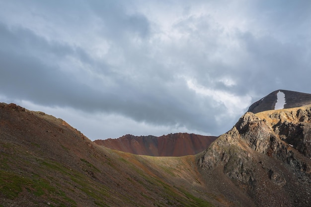 灰色の曇り空の下に広く鋭い山の尾根を持つ劇的な高山の風景 曇天の灰色の空に雨雲の下、尾根の頂上に大きな鋭い岩がある暗い雰囲気の山の風景