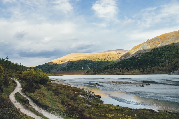 Dramatic autumn landscape with reflection of golden sunlight in water stream to mountain lake with view to motley hills. Autumn scenery with mountain creek in gold sunshine and multicolor mountains.