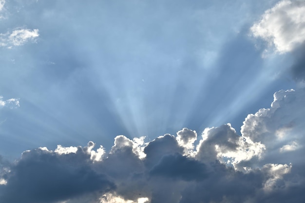 Dramatic blue sky with sun piercing through white fluffy clouds creating sunbeams
