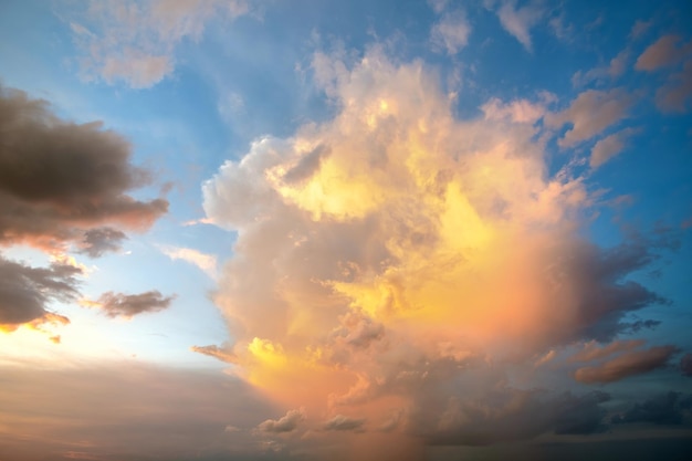 Dramatic cloudscape with puffy clouds lit by orange setting sun and blue sky.