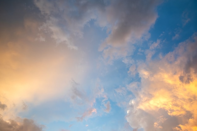 Dramatic cloudy sunset landscape with puffy clouds lit by orange setting sun and blue sky