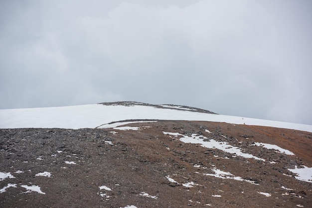 Dramatic landscape with huge rock mountain with snowy mountain dome under gray cloudy sky Awesome scenery with high snow mountain in dome shape in center at overcast weather Dome shaped mountain top